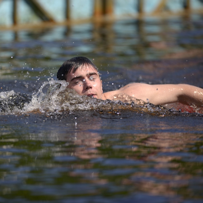 Person swimming freestyle in a body of water, creating splashes around them, with a blurred background.
