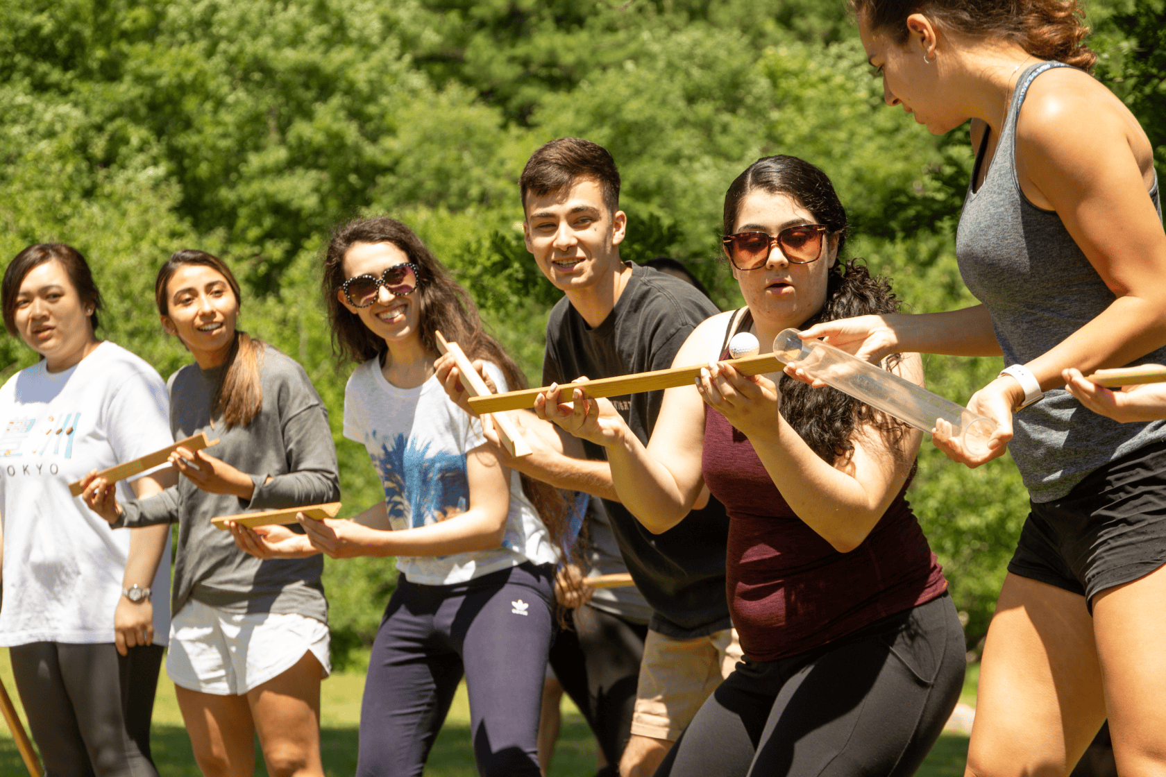 A group of people outdoors participate in a team-building activity, balancing a marble along wooden tracks.