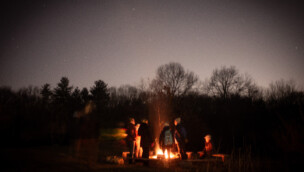 A group gathers around a campfire under the stars at night.
