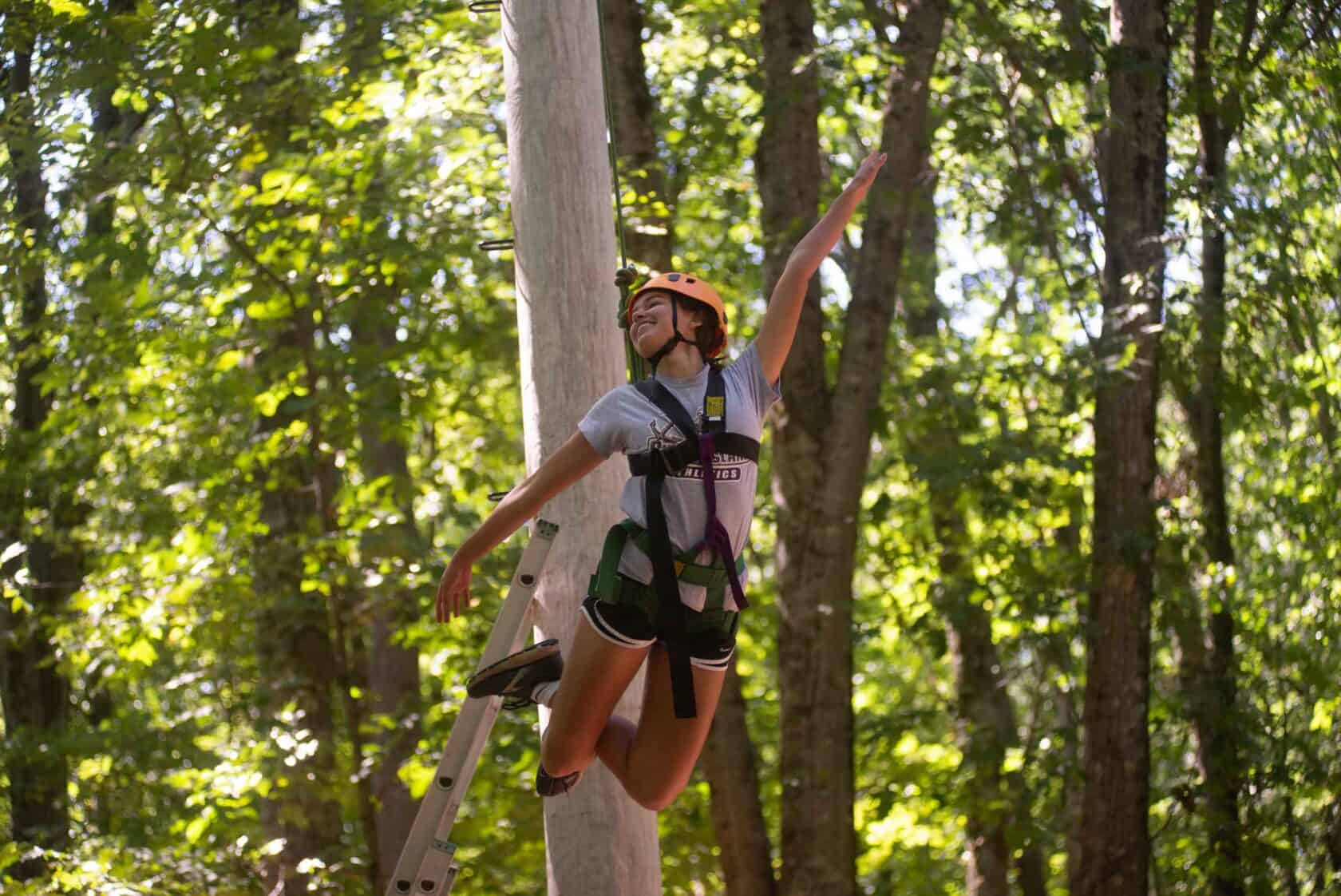 Girl hanging on harness ziplining through the woods.