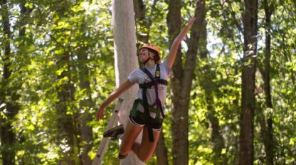 Girl hanging on harness ziplining through the woods.