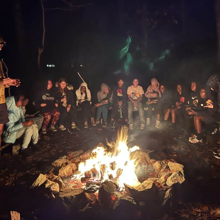 Middle school students gather around a fire on an overnight camping trip.