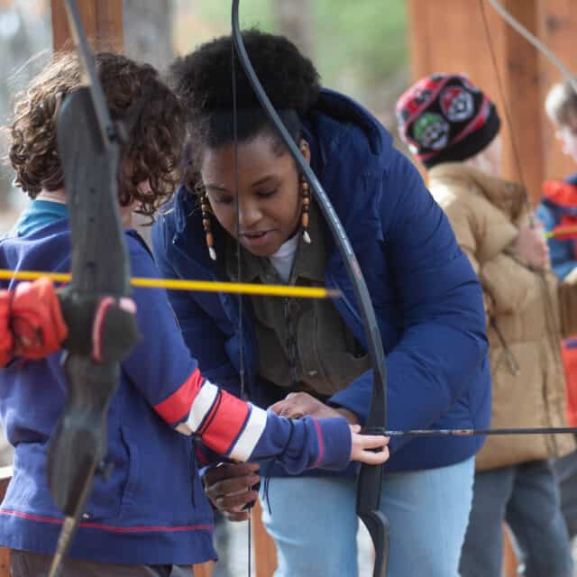 Hale staff member helping camper with bow during archery program.