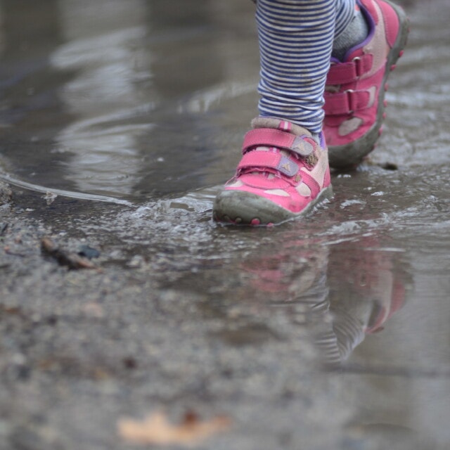 A child steps in a mud puddle on her way to the bus.