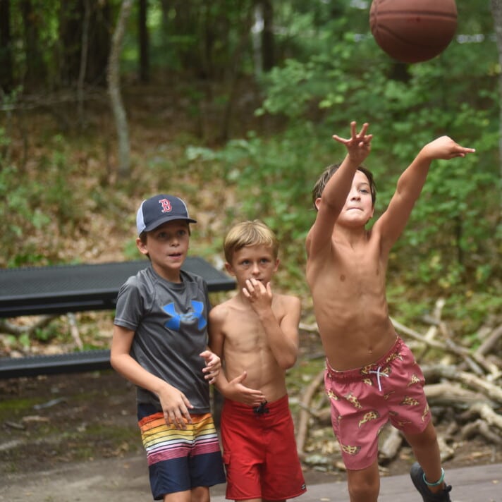 Three boys playing with a basketball in the woods.