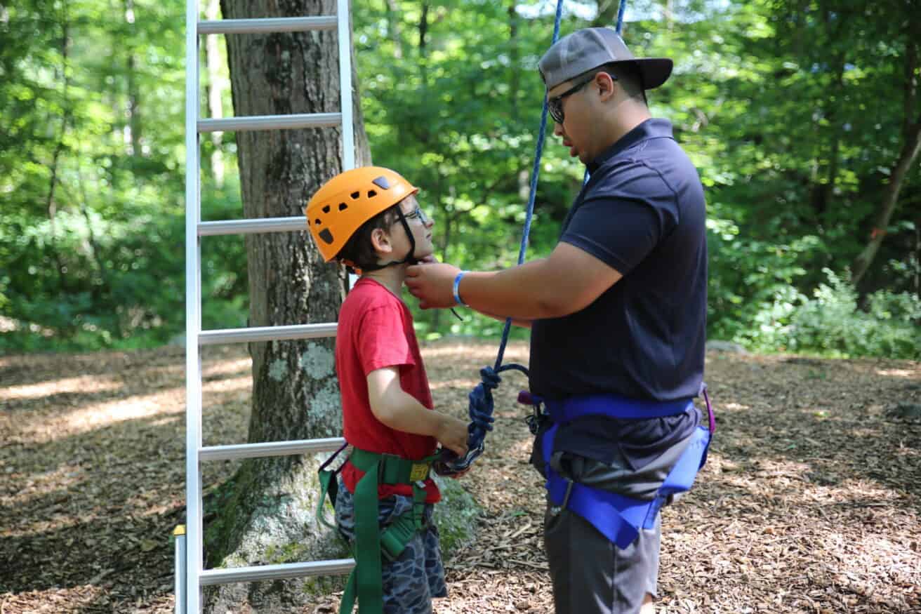 Facilitator helps a climber secure his helmet on ropes course.