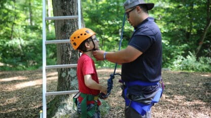 Facilitator helps a climber secure his helmet on ropes course.