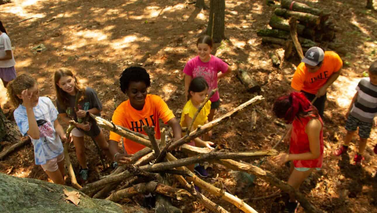 Campers stacking large sticks in a fire pile.