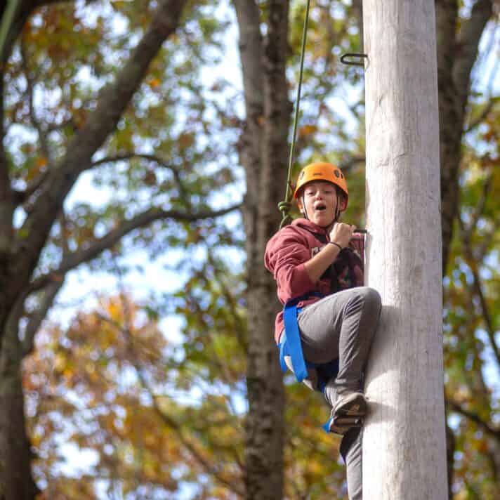 A participant climbs a poll on a ropes course.