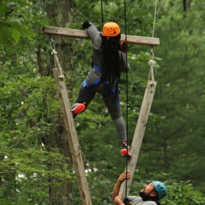 Two climbers help each other on a ropes course.