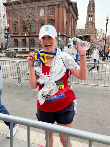 Cheerful Boston Marathon runner holding up medal.