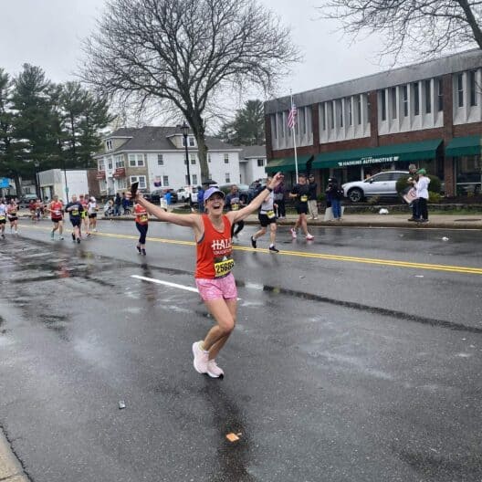A Boston Marathon runner raises her hands in victory