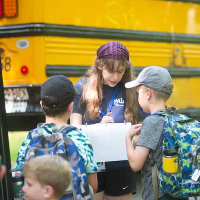 A group of children standing in front of a school bus with a counselor.