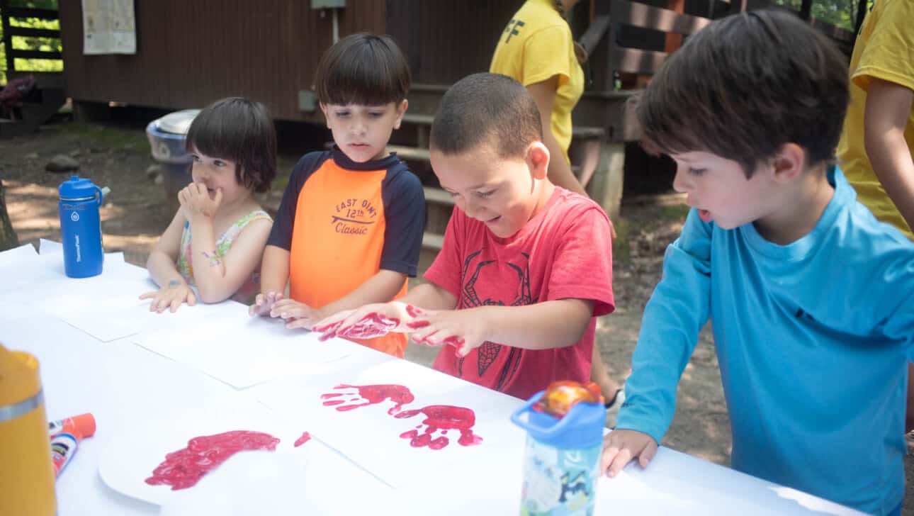 A group of children are painting with red paint on a table.