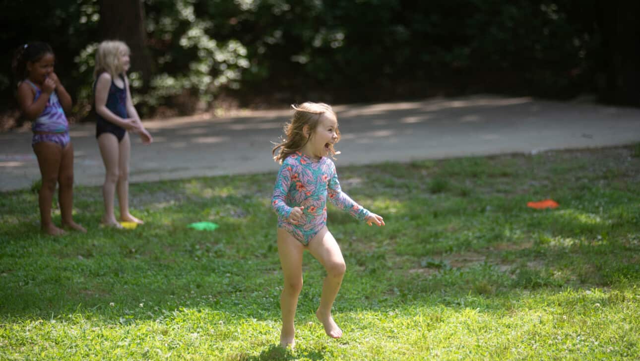A young girl in a swimsuit running in the grass.