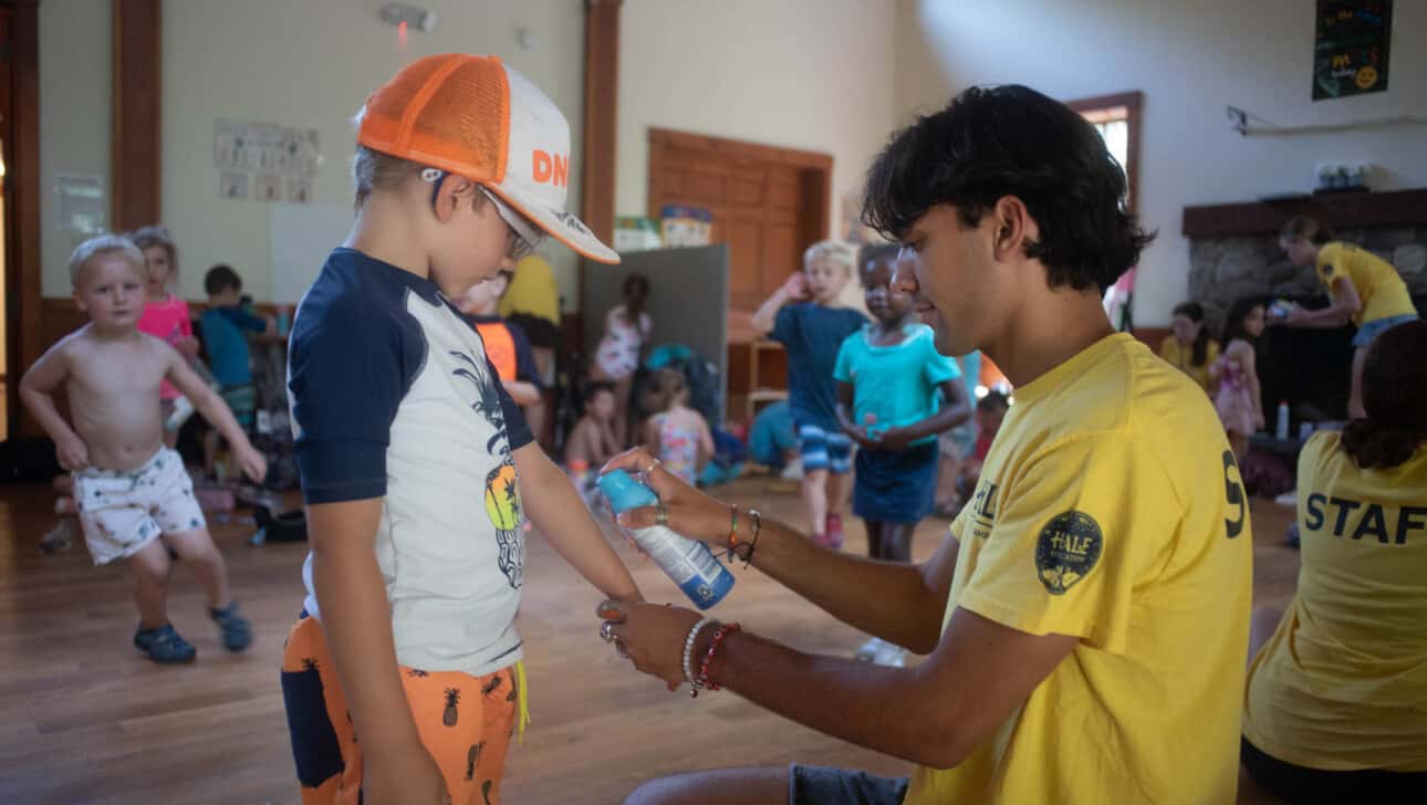 A counselor is helping a camper apply sunscreen.