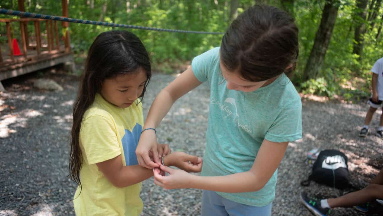 A girl is helping put a bracelet on a little girl's arm.