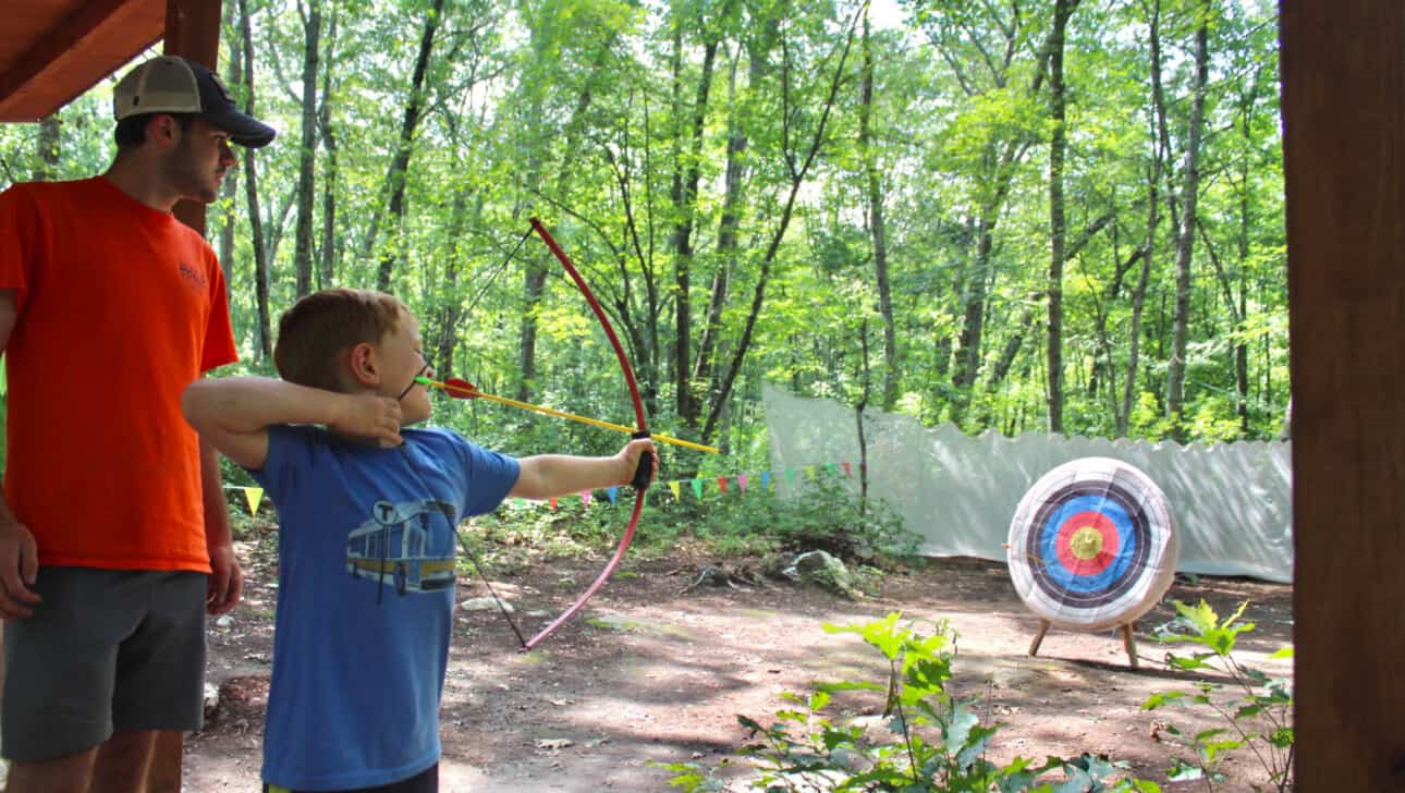 A counselor and camper aiming at an archery target.