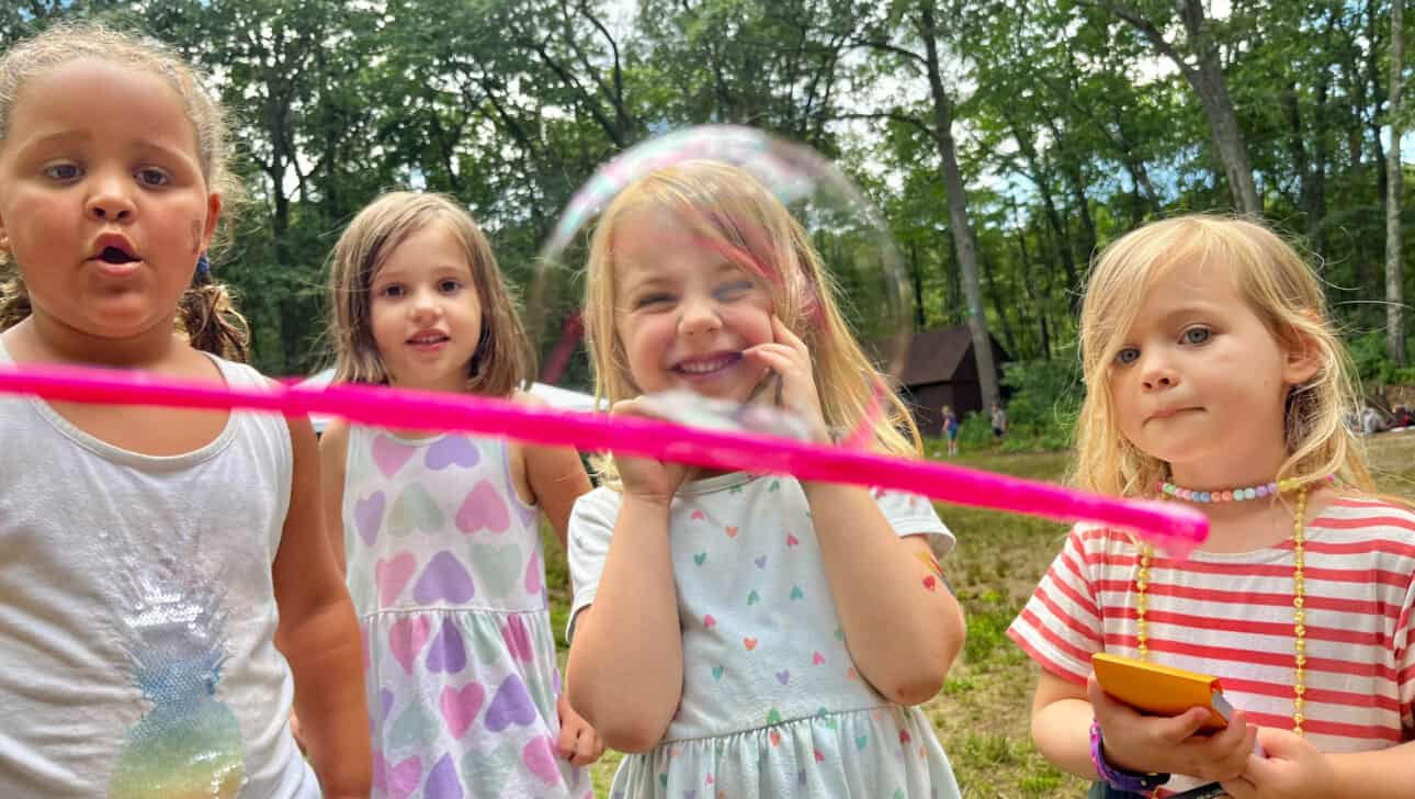 A group of girls playing with soap bubbles in the woods.