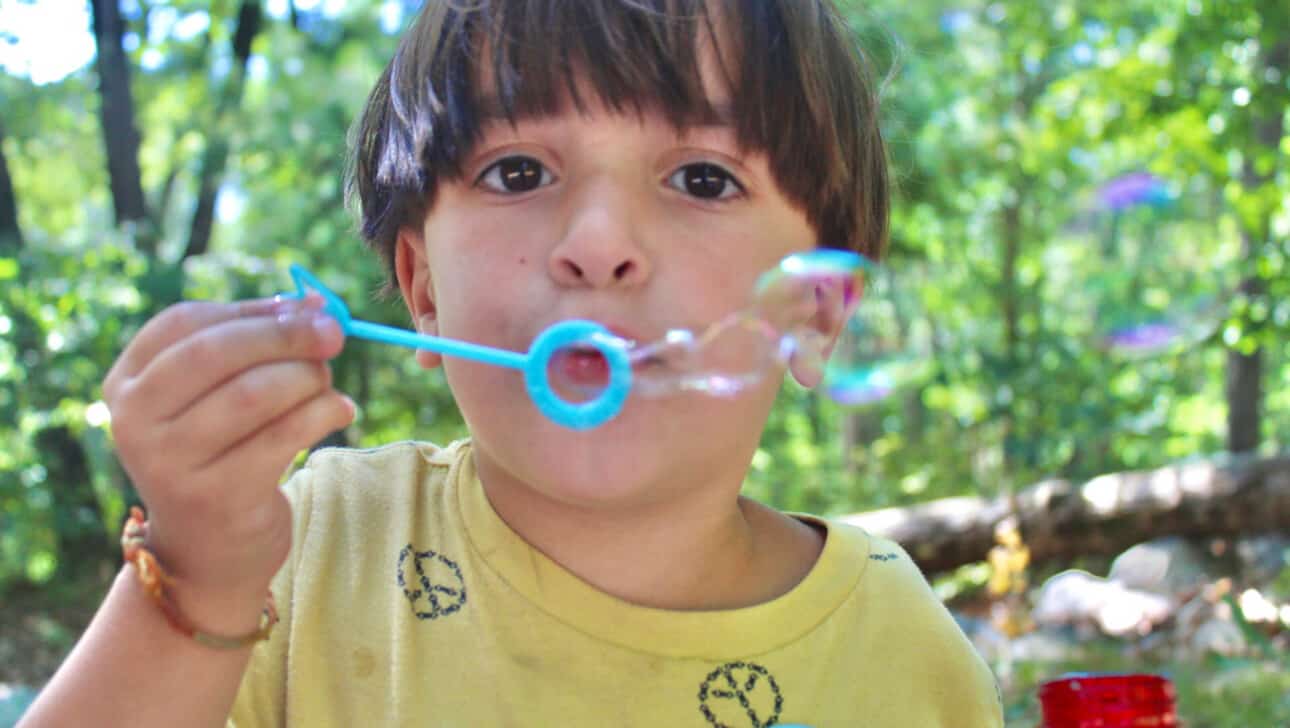 A young boy blowing soap bubbles in the woods.