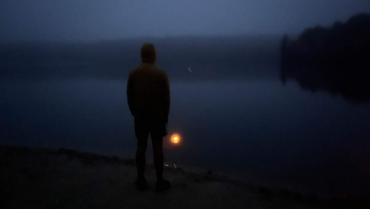 Person standing on a dock at night looking at the lake.