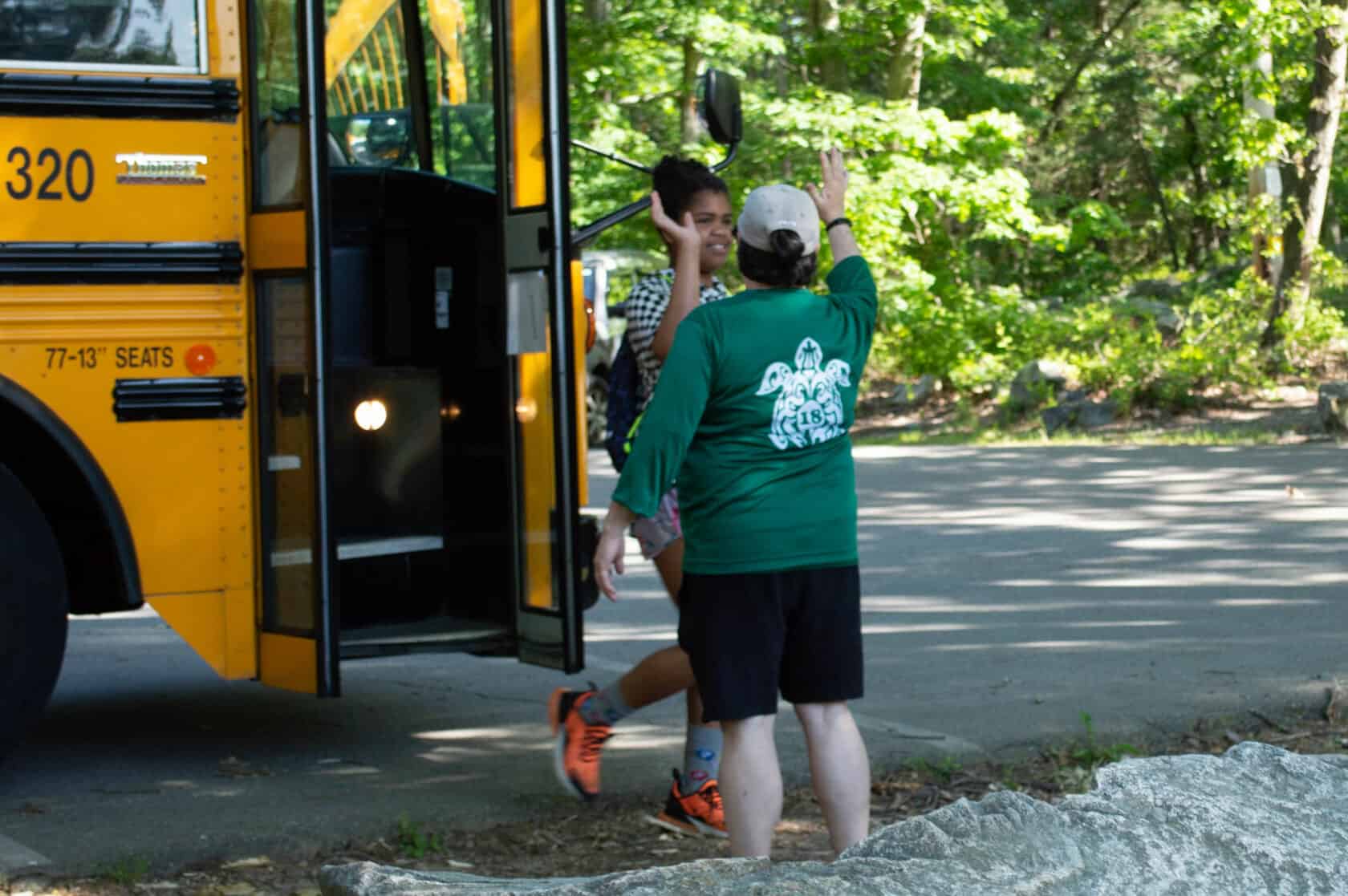 Staff member giving high-five to kid walking off the bus.