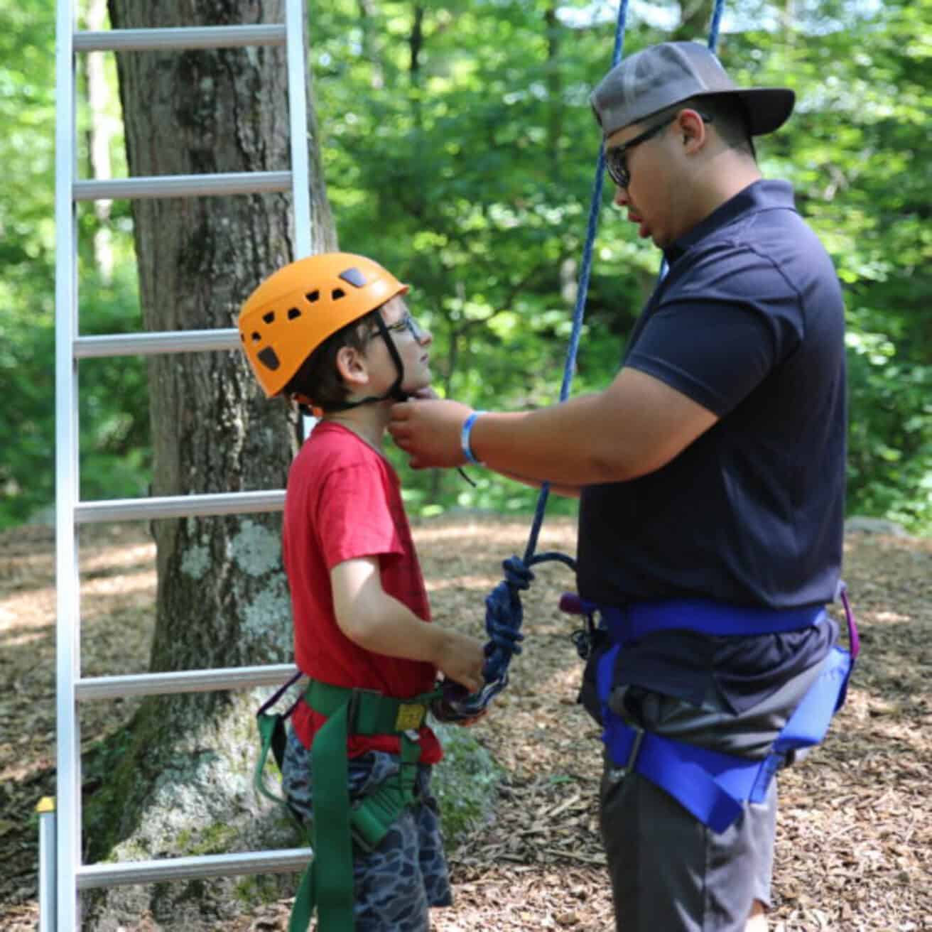 Facilitator putting a helmet on a camper for rock climbing.