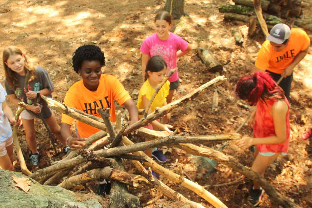 Counselor building a structure out of large branches with campers.