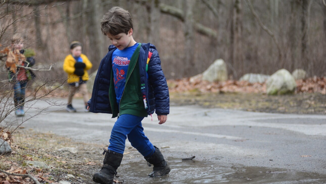 A child wearing rain boots walks through a mud puddle
