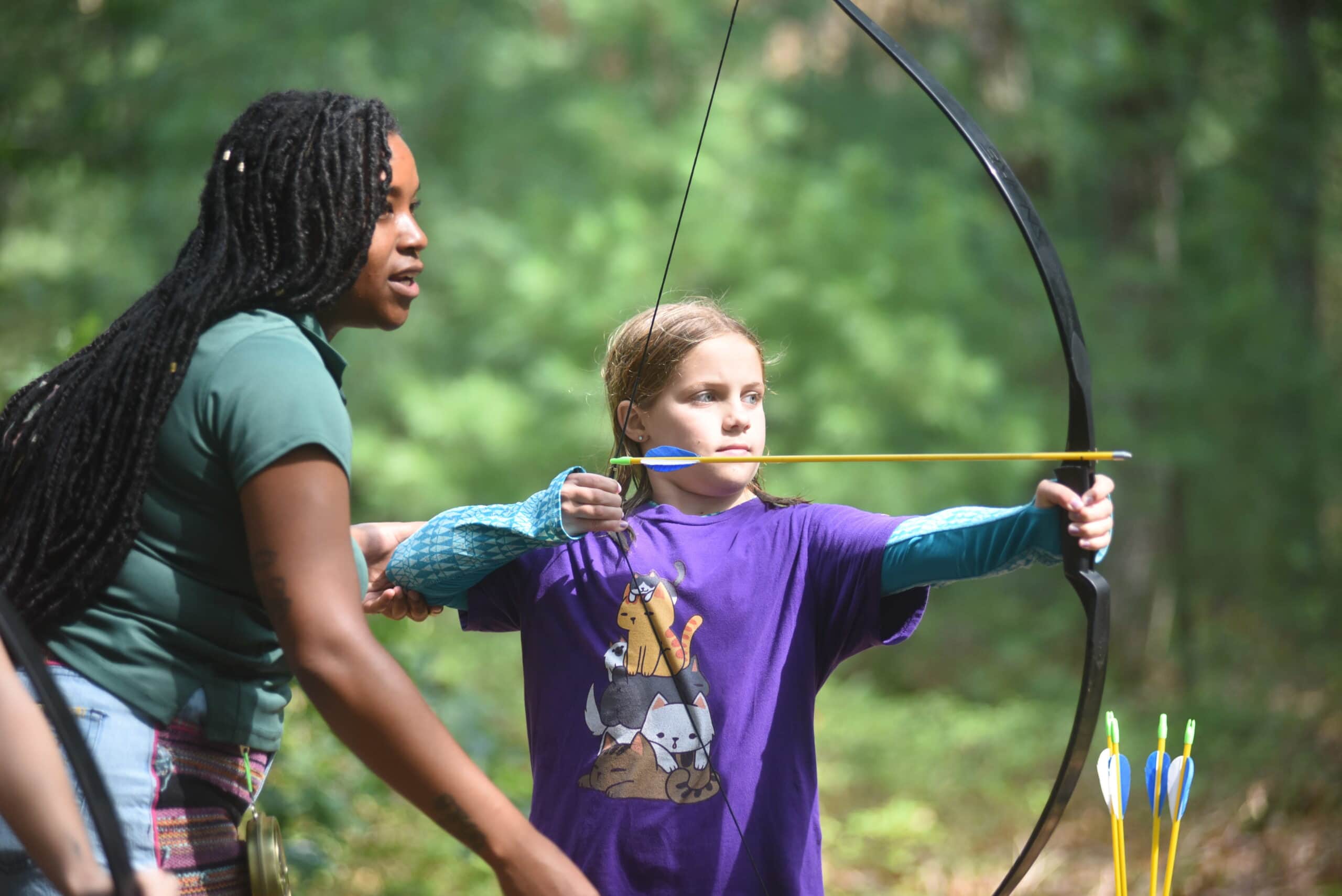 An archery instructor teaches a young student to shoot a bow and arrow.