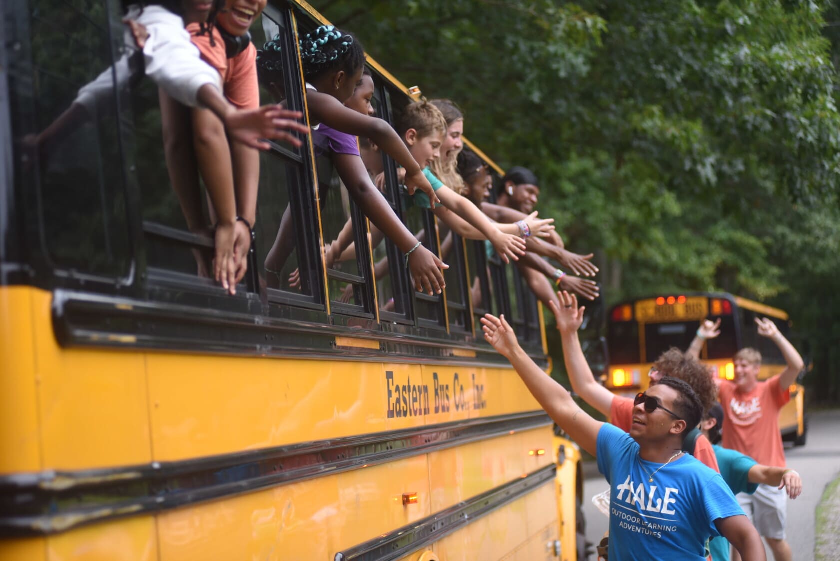 A counselor high-fives campers on a bus.