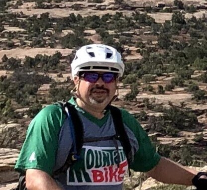 A man wearing a helmet and smiling on a biking trail.