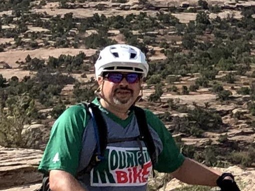 A man wearing a helmet and smiling on a biking trail.