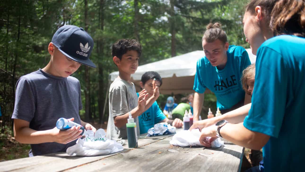 A group of campers at a table in a wooded area.