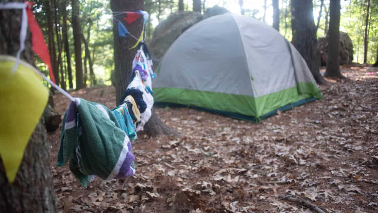 A tent with clothes hanging on a line in the woods.