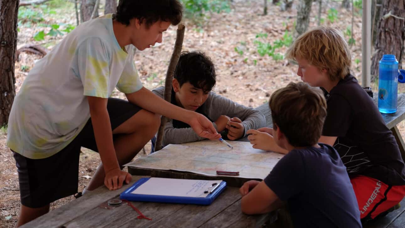 A group of boys looking at a map in a wooded area.