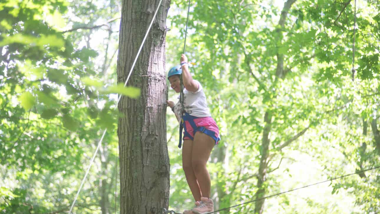 A girl on a ropes course in the woods.