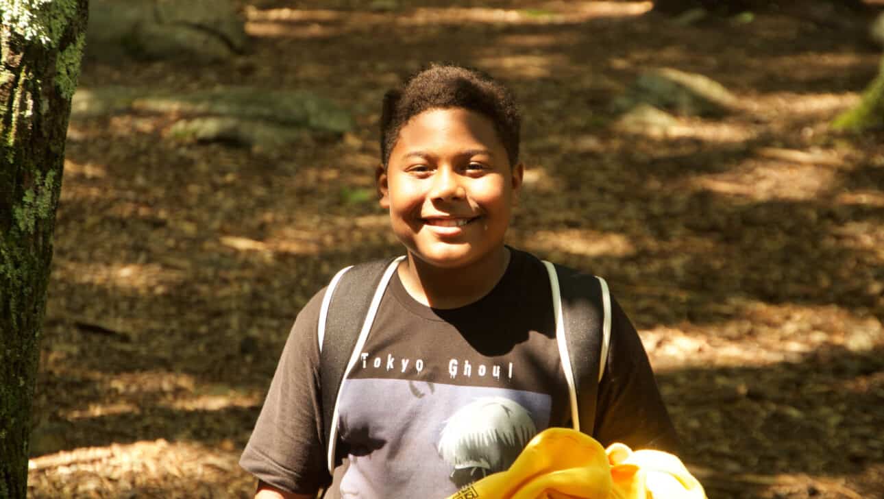 A boy smiling and walking in the woods.