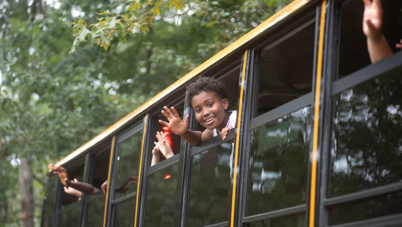 A group of children on a school bus waving.