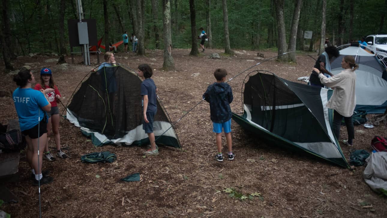 A group of people setting up tents in a wooded area.