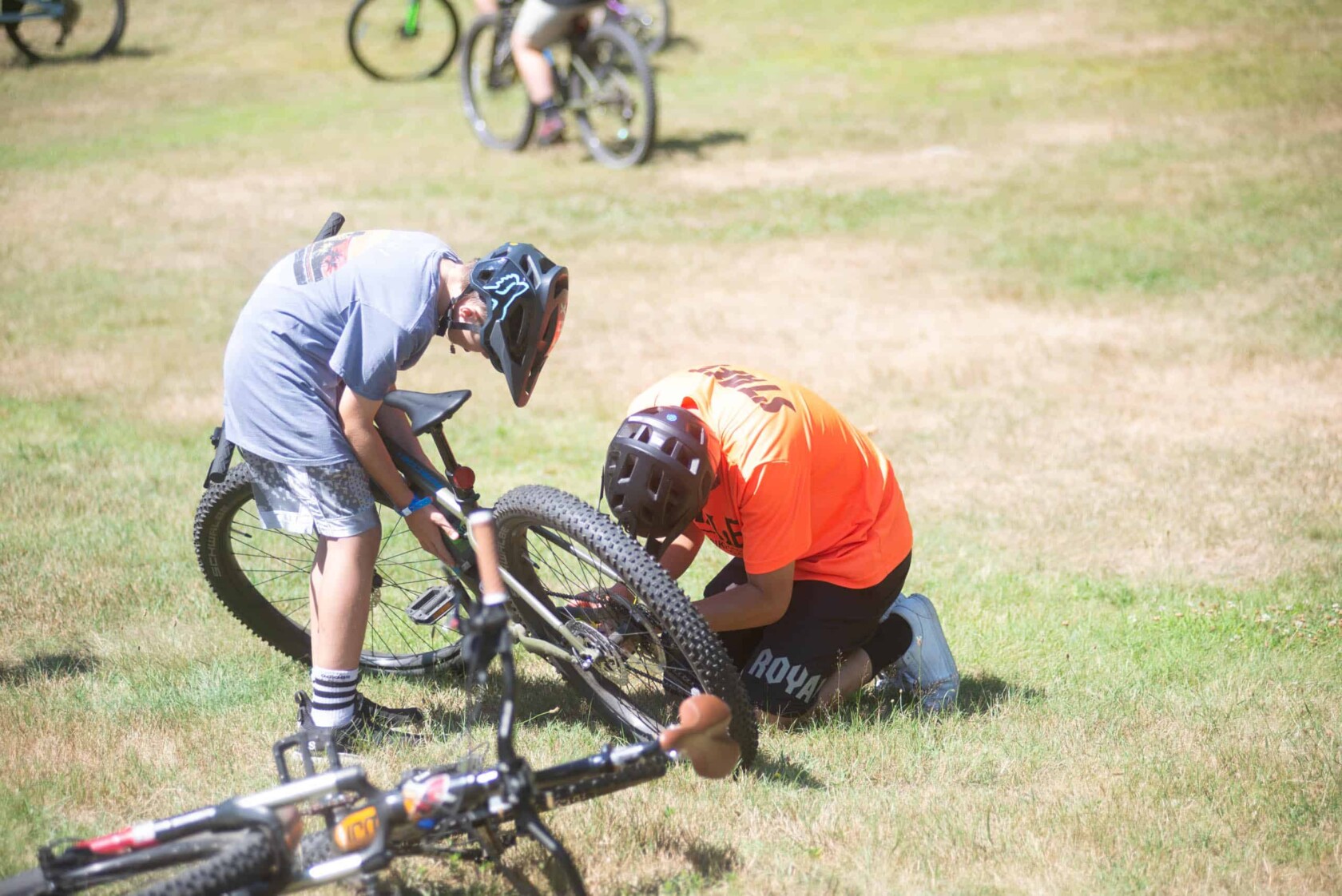 A group of people fixing a bike in the grass.