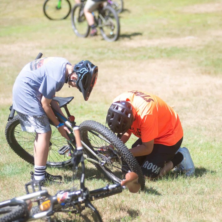 A group of people fixing a bike in the grass.