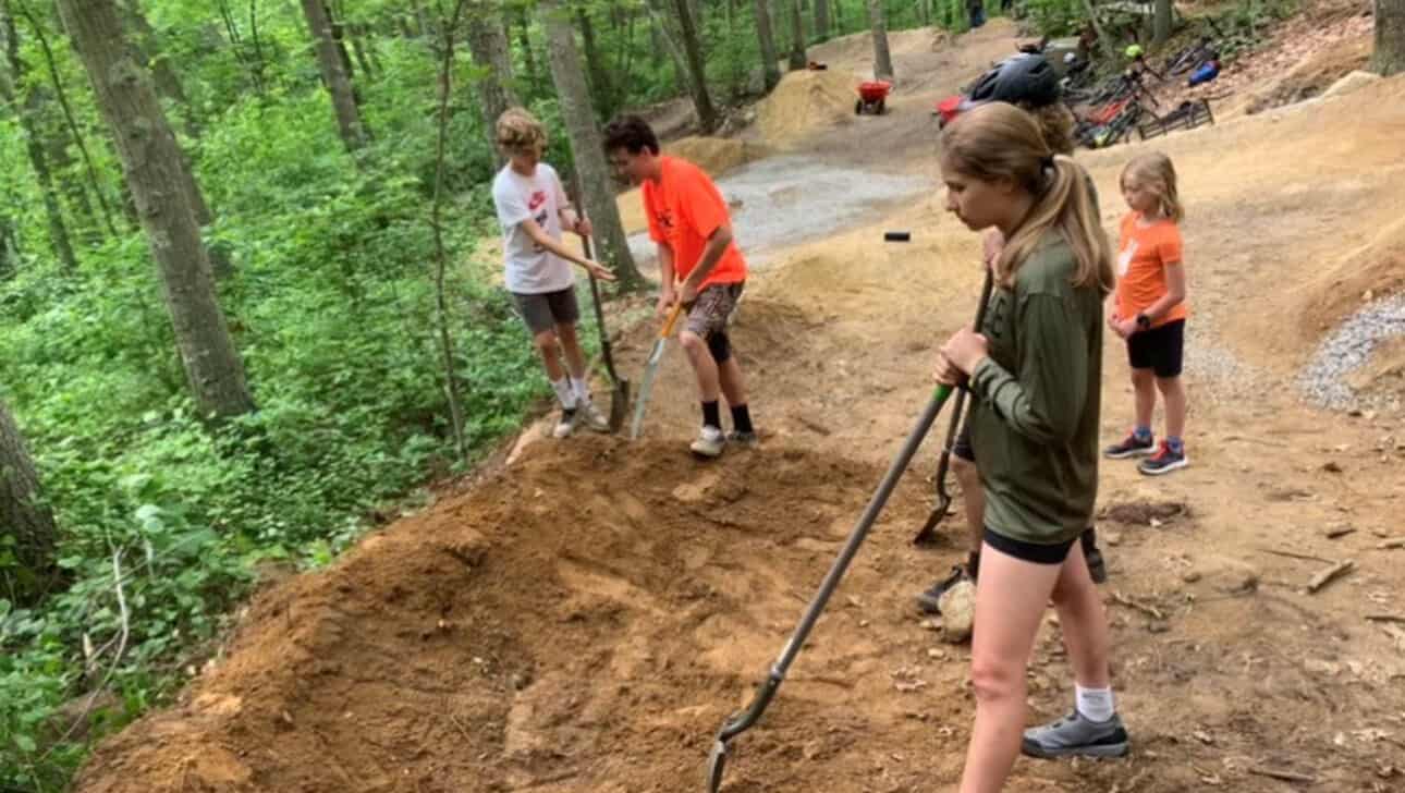 A group of kids working on a dirt trail in a wooded area.