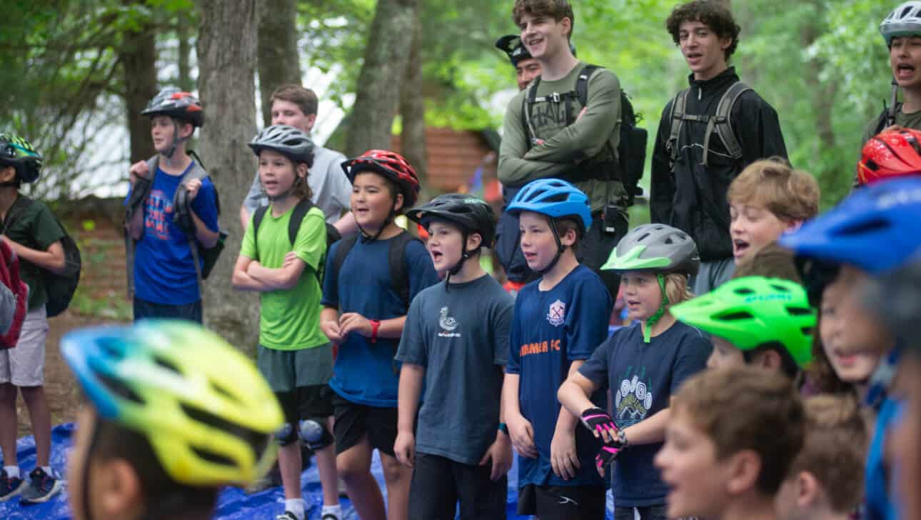 A group of children wearing helmets in a wooded area.