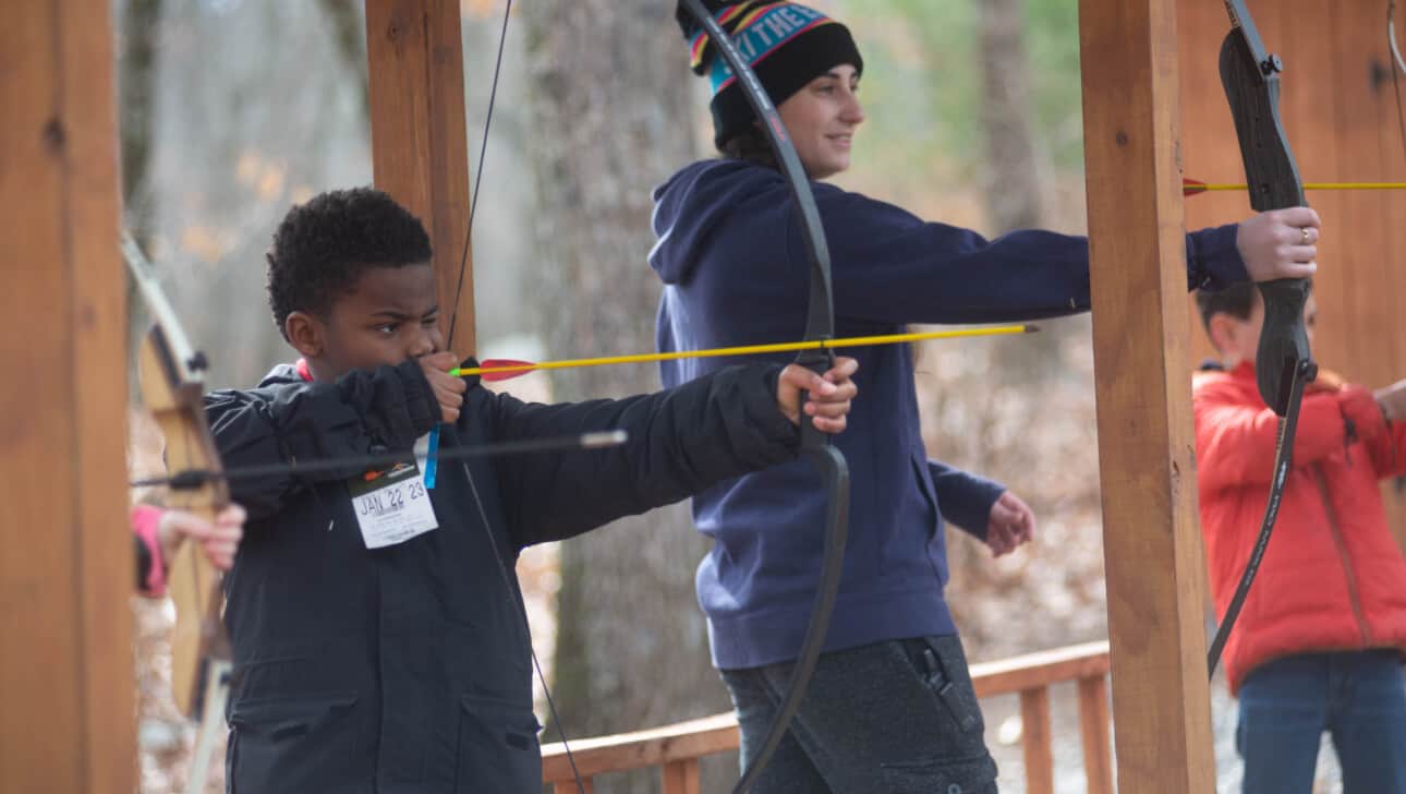 A group of young people practicing archery in a wooded area.