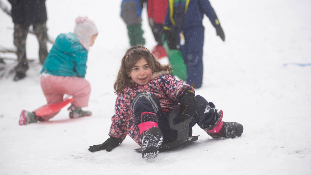 A little girl is sledding down a snowy hill.