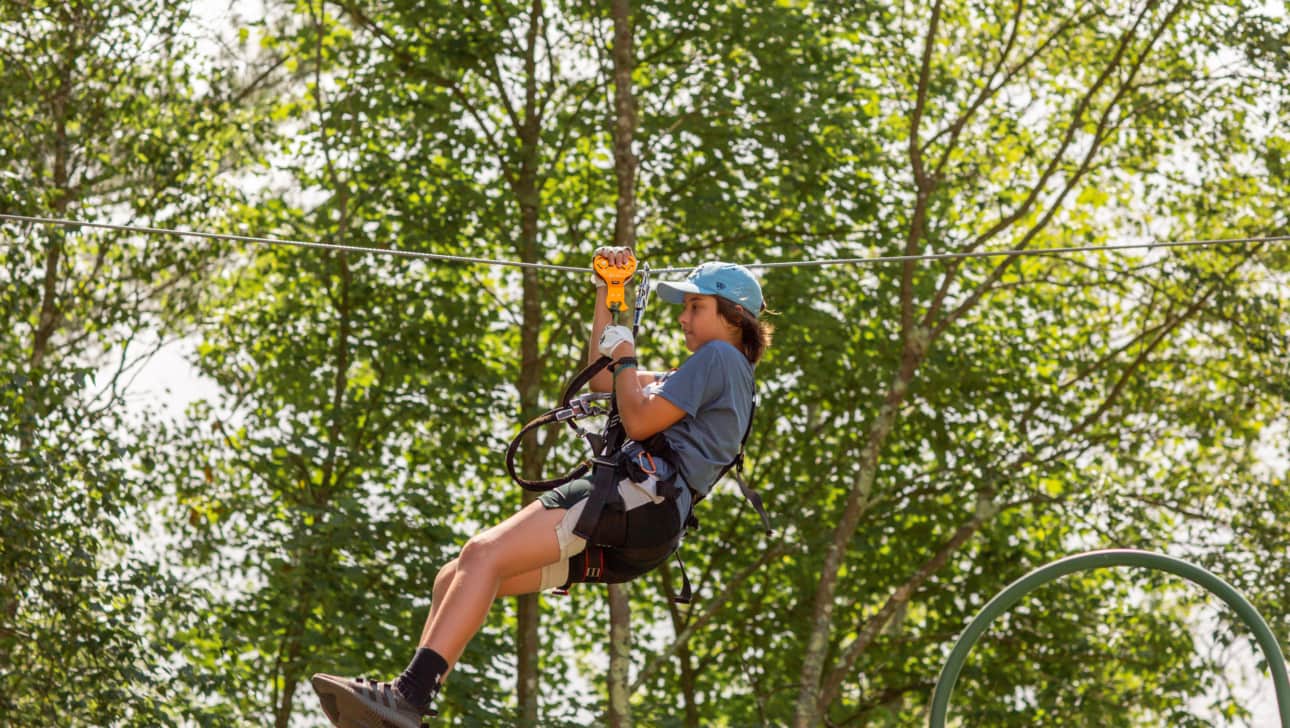 A young person zip-lines on a challenge course.