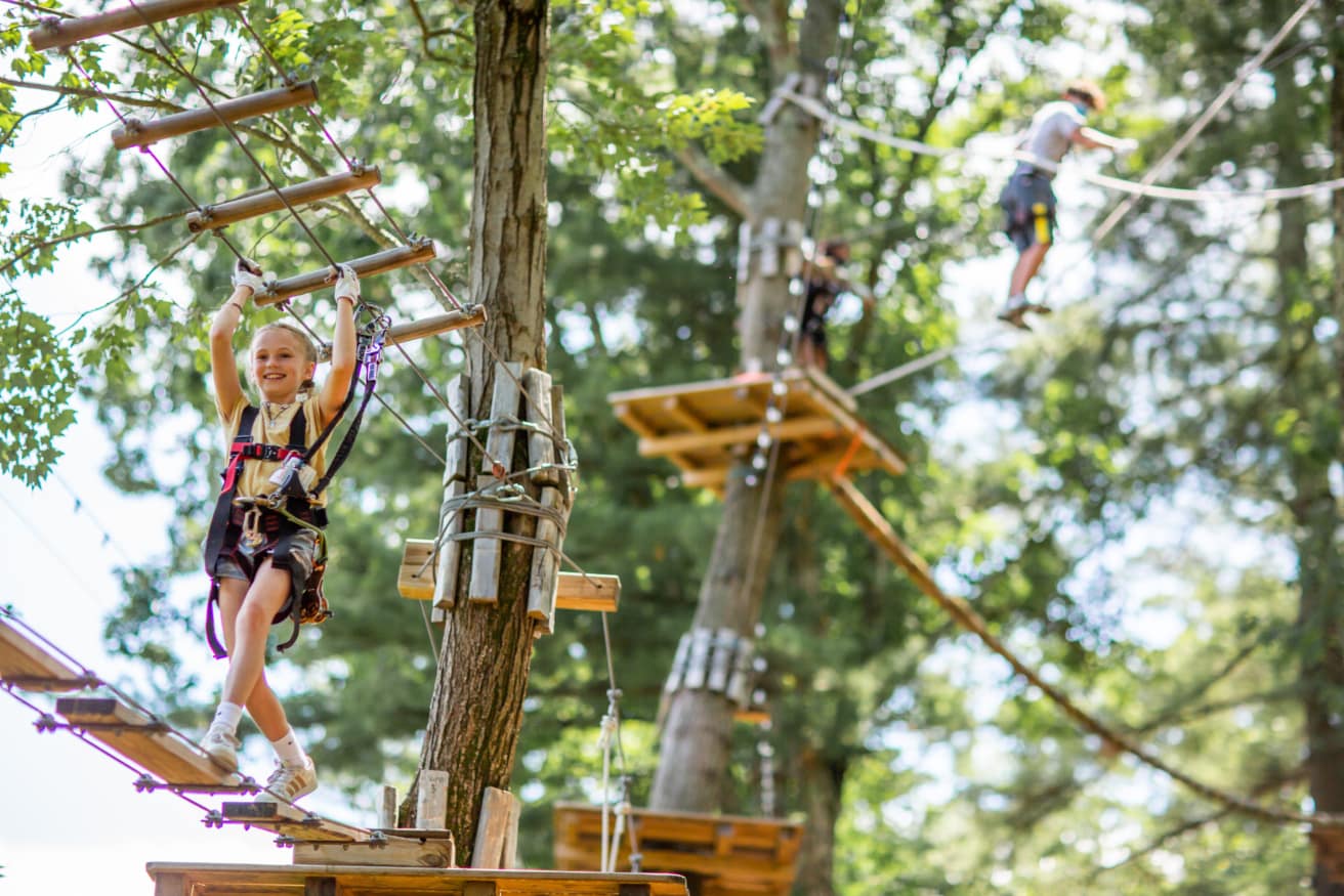 A young girl smiles as she crosses a high ropes element on a challenge course.