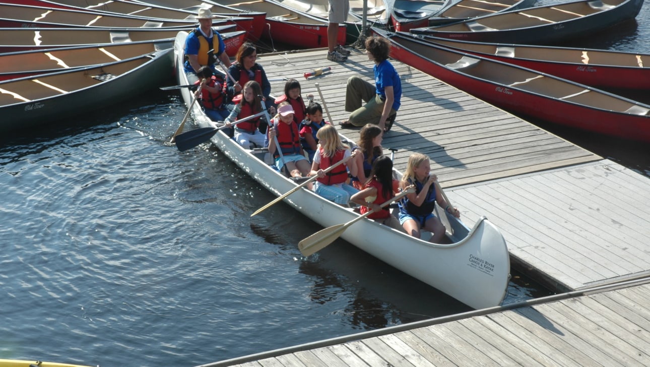 A group of children in a canoe prepares to paddle on a river.