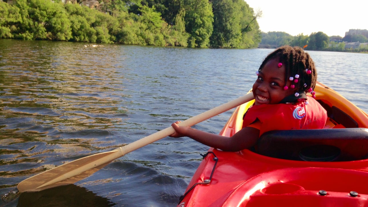 A young girl learns to paddle in a tandem kayak.